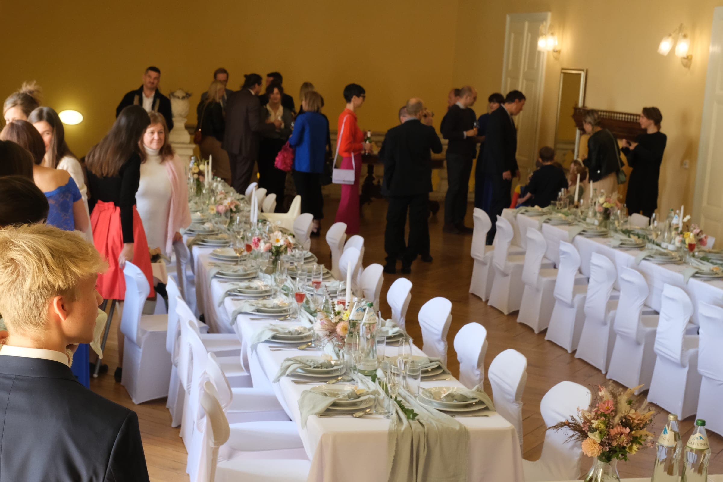 Svatební hostina v sále — dlouhé bíle prostřené tabule a hosté