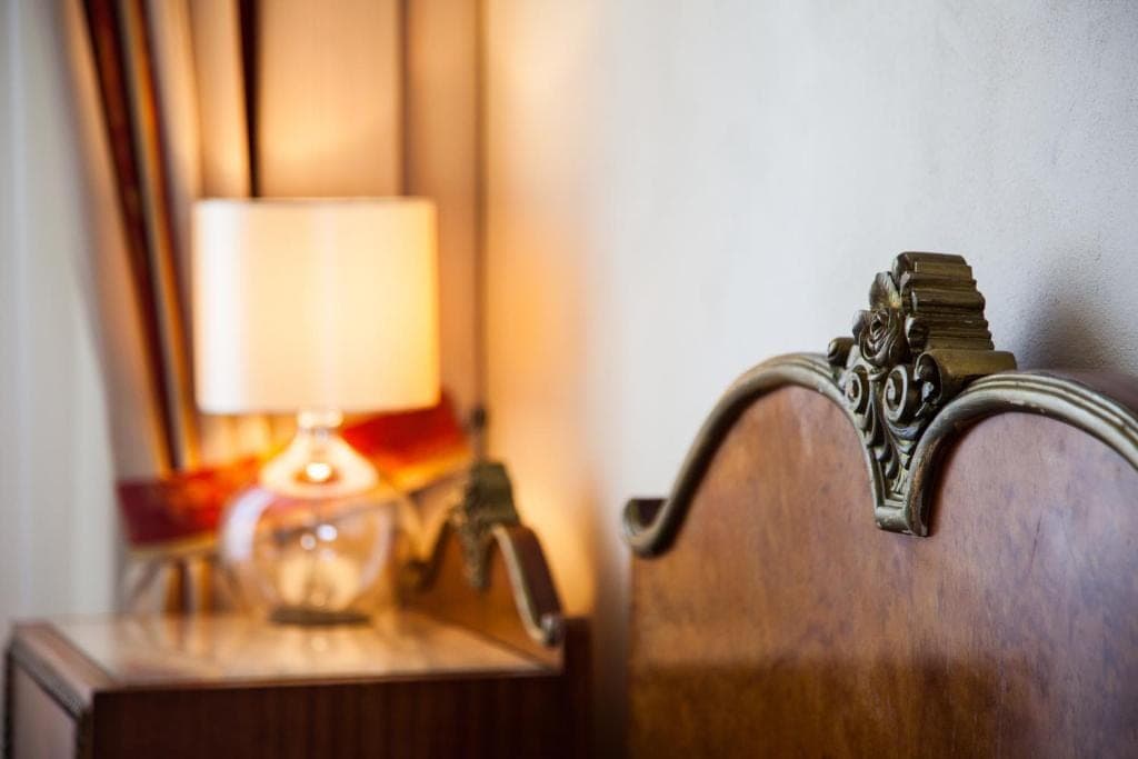 Detail pokoje — stolní lampa a vyřezávané čelo dřevěné postele