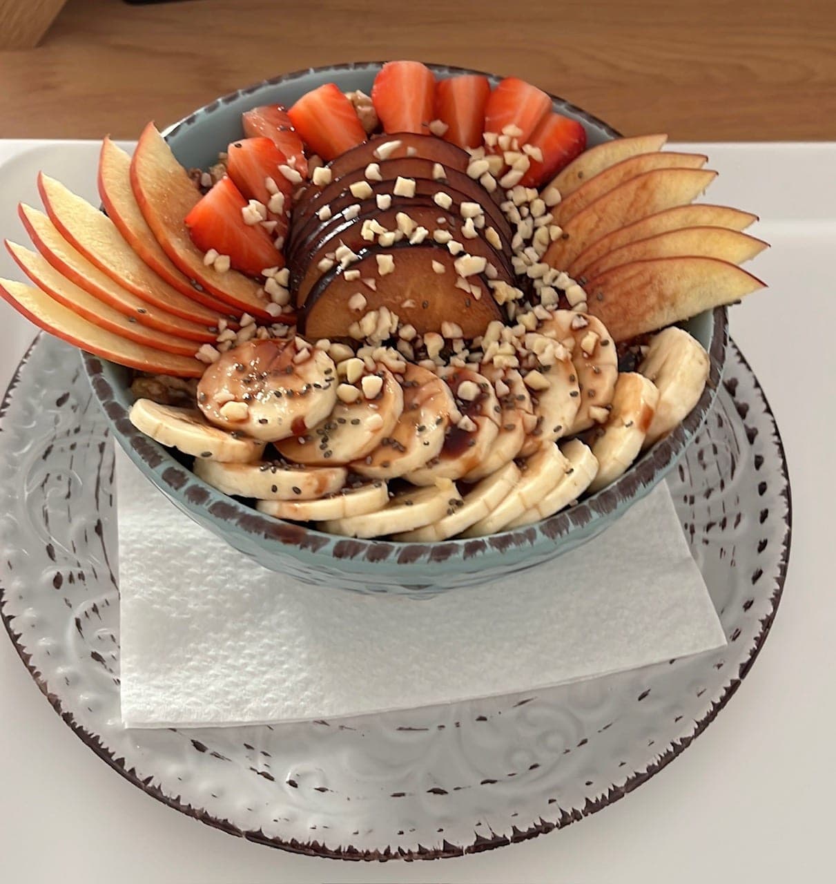 Eine Schale mit Bananenscheiben, Erdbeeren, Zwetschge, Apfelfächer, Chiasamen und gehackten Nüssen