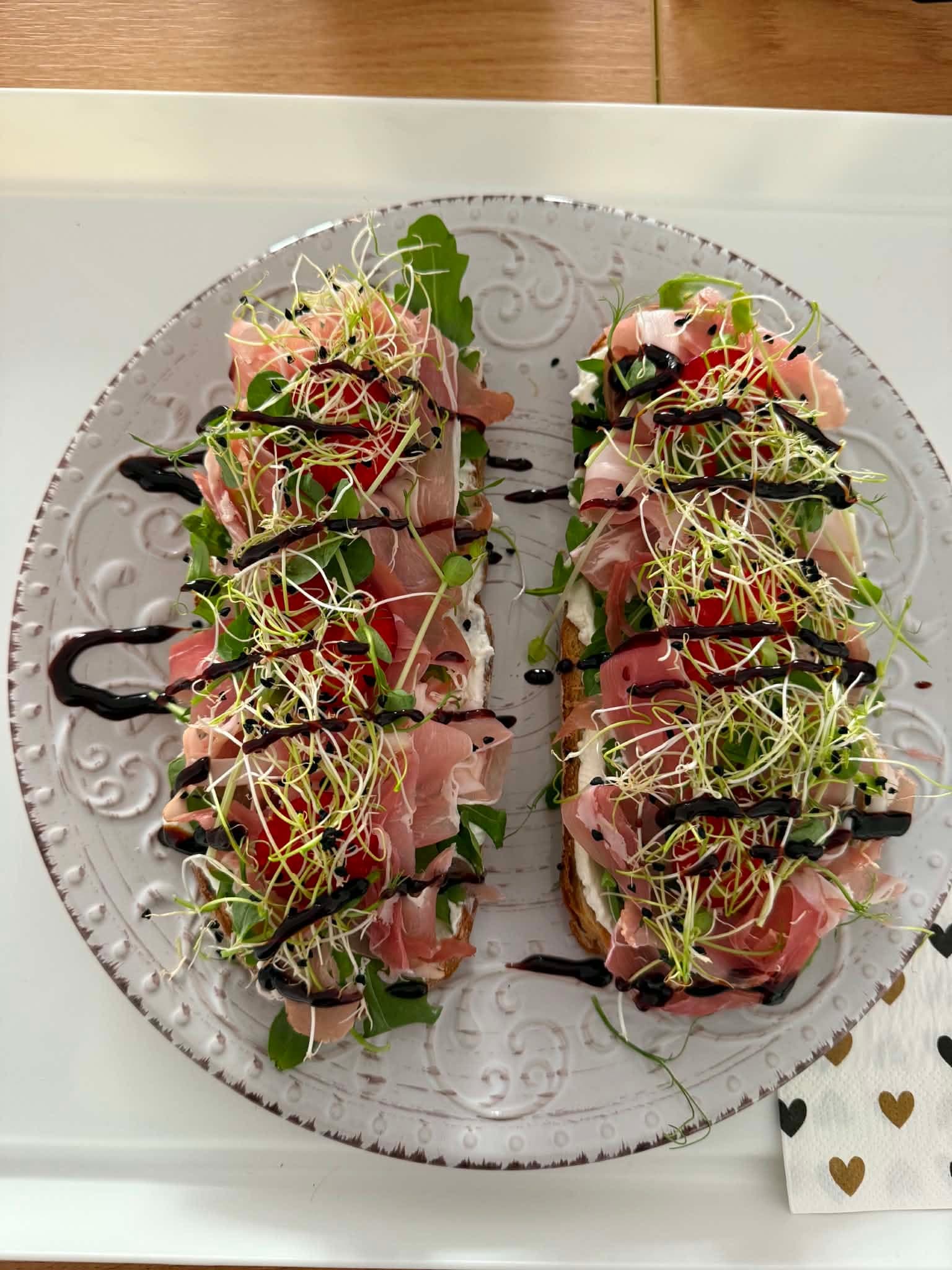 Zwei belegte Brote mit Frischkäse, Prosciutto, Tomaten, Sprossen und Balsamico